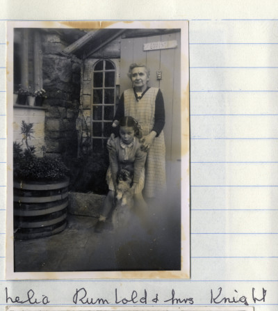 Older woman and child with dog outside a house and shed