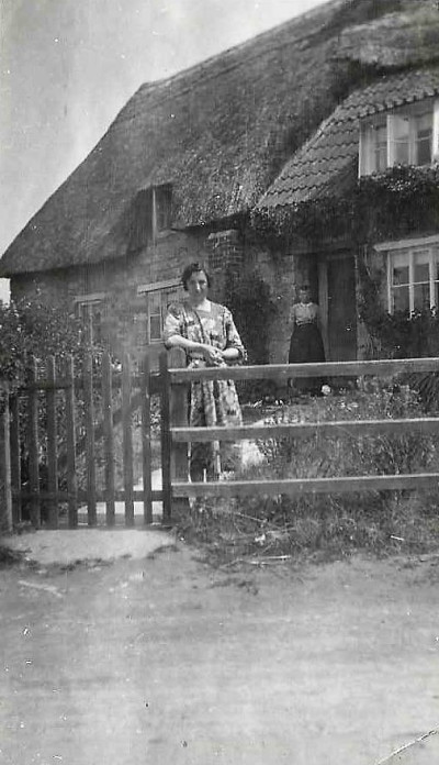 Two women outside thatched cottage.