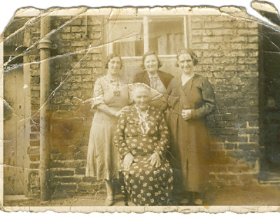Four women sat outside of brick house.