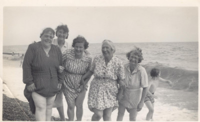 Five women at the seaside with dresses rolled up.