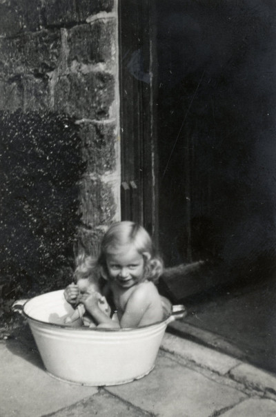 Child and doll in tin bath on door step