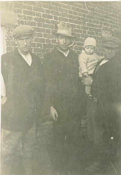 Three men in working clothes with baby.