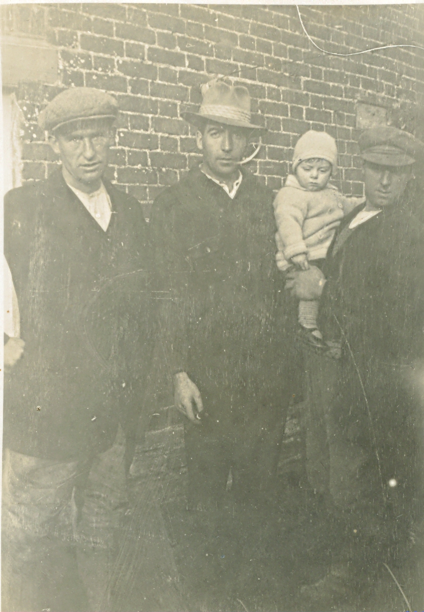 Three men in working clothes with baby.