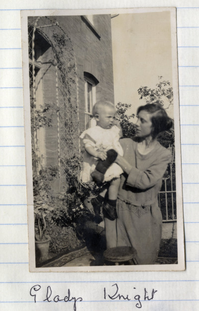 Young woman holding baby outside house.