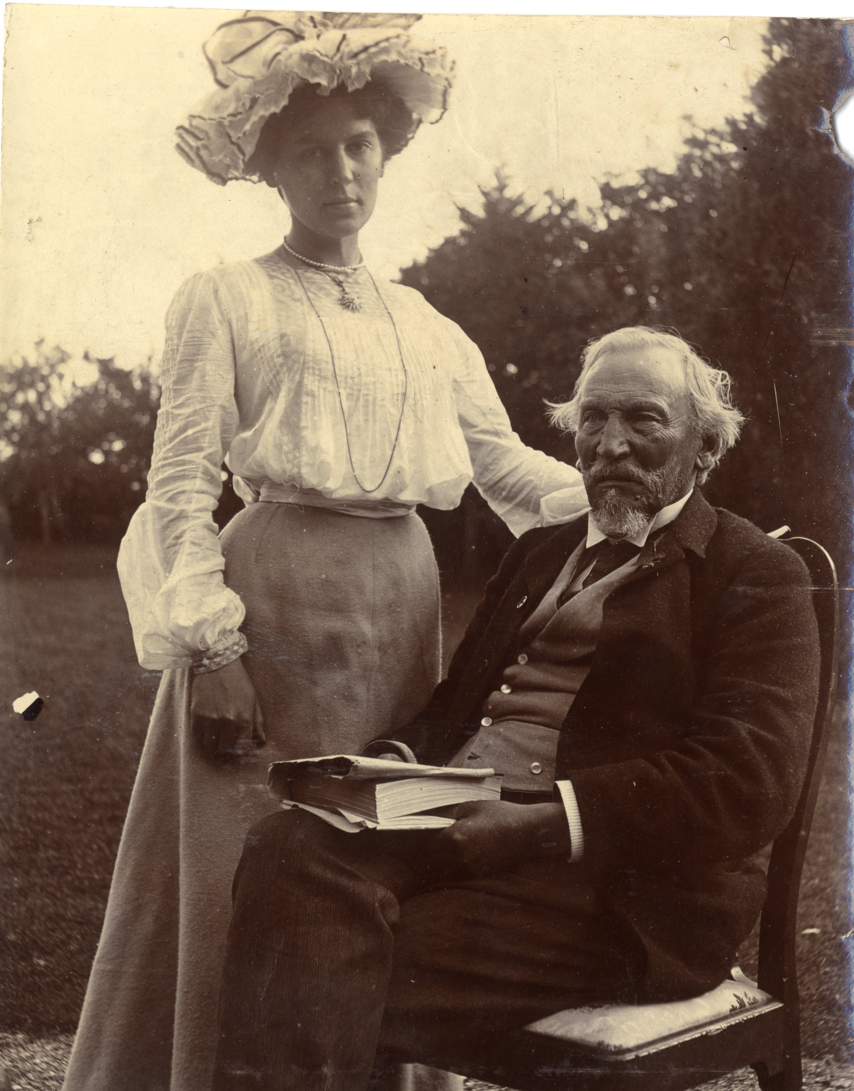 Mabel Bradford possibly, in fine clothes in garden with elderly man