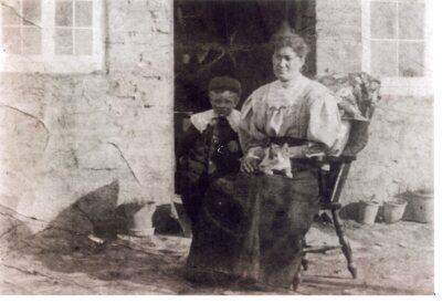 Woman seated and young boy, outside cottage